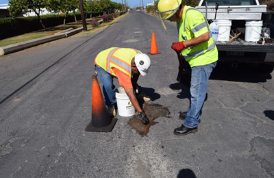 Asphalt repair patching pothole on road in Honolulu by two men crack-fill.png